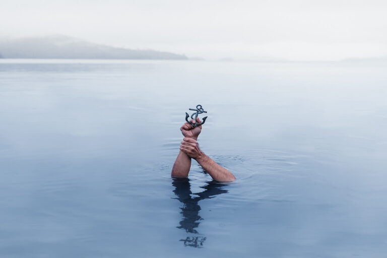 Jemand verschwindet unter Wasser und hält nur noch den Anker über der Wasseroberfläche. Als Metapher für 'Change in der der Unternehmenskultur verankern'