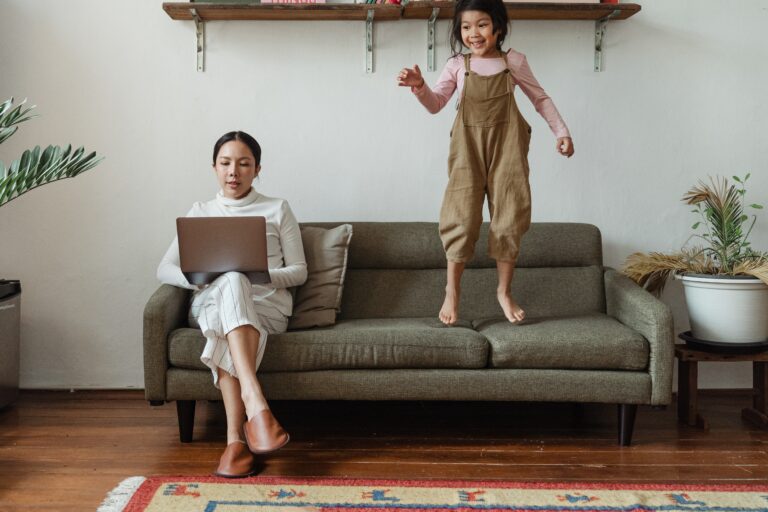 Eine Mutter mit Laptop und Tochter auf dem Sofa, die im Home-Office überlebt und arbeitet