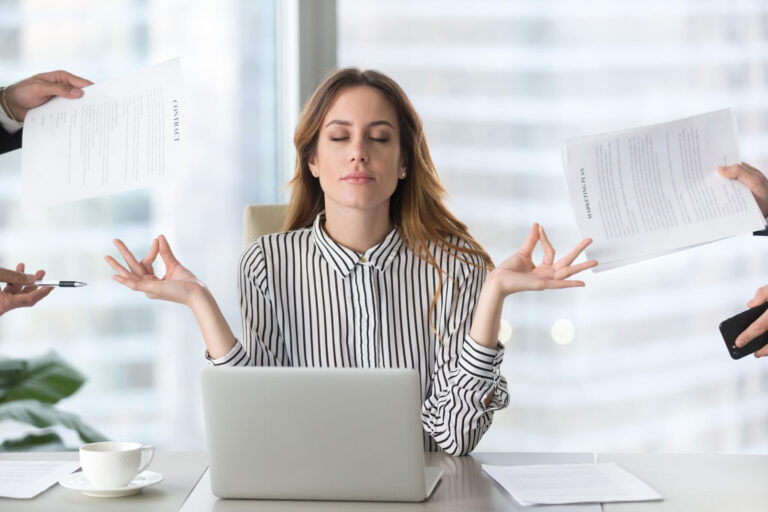 Eine Frau am Schreibtisch vorm Laptop meditiert. Sie sieht überfordert aus. Titelbild für den Artikel 'Wie du deine Zeit optimieren kannst'