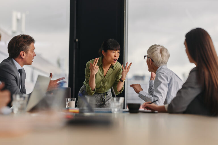 Zwei Frauen am Ende eines Konferenztisches in hitziger Diskussion – Symbolbild für Konflikte am Arbeitsplatz, bzw. Konflikte im Job